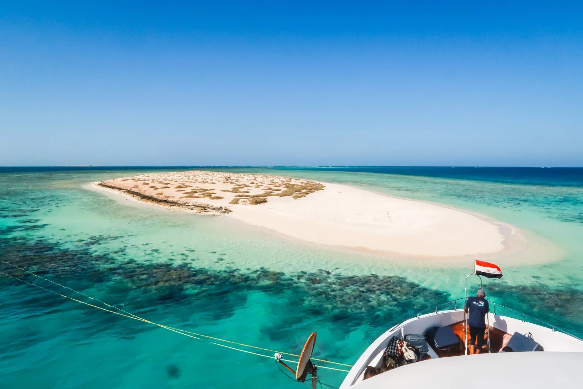 View from the yacht's deck towards a sandy sandbar island in turquoise water